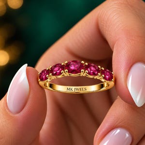 May include: A gold band ring featuring five round, vibrant pinkish-red gemstones set in a row. The metal band is polished yellow gold and includes the engraved text MK JWELS on the inner surface, visible between the gemstone settings.