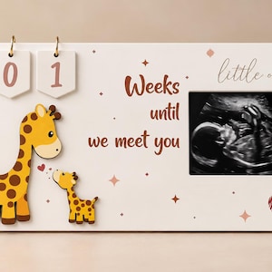 Puede incluir: Un letrero de cuenta regresiva rectangular de madera blanca con dos etiquetas colgantes numeradas que muestran 01, una ilustración de una jirafa y su cría, y el texto Weeks until we meet you little one. Incluye una imagen de ecografía en blanco y negro.