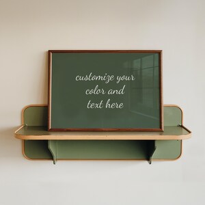 Könnte beinhalten: Ein rechteckiger Bilderrahmen mit dunklem Holzrahmen und dunkelgrünem Hintergrund mit dem weißen Text "customize your color and text here", der auf einem wandmontierten olivgrünen Regal mit abgerundeten Kanten steht.