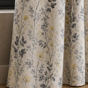 Puede incluir: Un par de cortinas de cuerpo entero con un fondo beige claro y un estampado botánico repetitivo. El patrón consiste en tallos delgados con hojas de color gris oscuro y pequeñas flores amarillas, creando un diseño vertical inspirado en la naturaleza.
