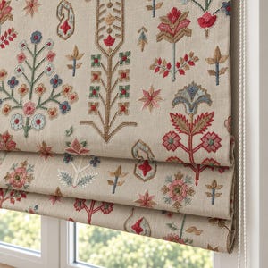 Puede incluir: Un estor plegable de tela beige con un intrincado patrón floral bordado en tonos rojos, azules, verdes y marrones. El cubrimiento de ventana incluye un mecanismo de cadena de cuentas blanca en el lado derecho para ajustar los pliegues.