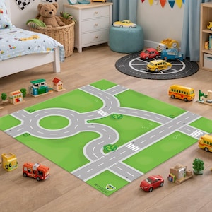 May include: A rectangular play rug featuring a printed road network with gray streets, white lane markings, a central roundabout, and green grassy areas. The design includes crosswalks and small green shrub illustrations on a flat surface.