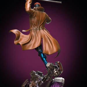 Puede incluir: Una figura coleccionable de un personaje con una gabardina larga marrón, guantes negros y mallas metálicas azules. La figura está en una postura dinámica, sosteniendo un bastón plateado largo sobre la cabeza y sobre una base mecánica detallada.
