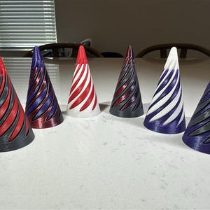 May include: Six conical objects with a spiraling, ribbed texture arranged in a row. The cones feature various two-tone color combinations, including red and gray, purple and metallic red, white and red, dark gray and red, white and purple, and gray and purple.