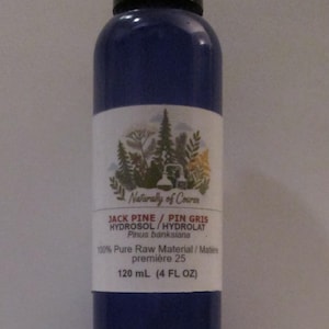 May include: A blue plastic bottle with a black cap containing Jack Pine hydrosol. The label features a forest illustration, the text Naturally of Course, Jack Pine / Pin Gris, Hydrosol / Hydrolat, Pinus banksiana, 100% Pure Raw Material, and 120 mL (4 FL OZ).