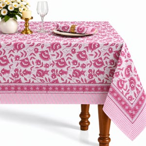 Puede incluir: Un mantel rectangular con base blanca y un patrón repetitivo de flores y hojas rosas. El borde incluye una banda decorativa con motivos florales pequeños y un acabado a rayas. Una servilleta a juego descansa sobre un plato.
