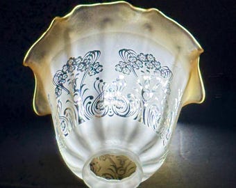 May include: A bell-shaped glass lamp shade with a ruffled, golden-tinted edge. The translucent body features a frosted finish and is decorated with a repeating dark floral pattern of stems and blossoms encircling the exterior surface.