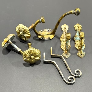May include: A collection of antique brass and metal hooks in various designs. The hooks include ornate, floral-shaped knobs, curved coat hooks, and decorative wall-mounted options. The metal has a weathered, aged appearance.