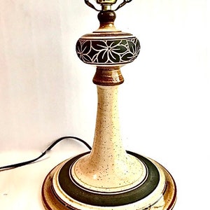 May include: A ceramic table lamp with a beige speckled base and a dark green and brown circular base. The lamp features a decorative floral pattern in white and dark green on the central globe. The lamp is approximately 20 inches tall.