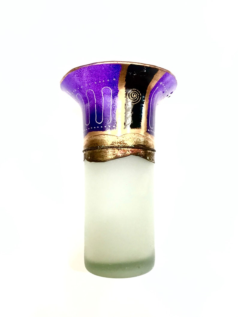 May include: A decorative glass bottle with a frosted body and a flared top. The top is decorated with purple, black, and gold designs. The bottle has a gold-colored metal band near the top.
