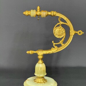May include: A gold-toned metal stand featuring a curved arm with ornate scrollwork and a small hanging hook. The base and central support are crafted from pale green onyx stone, accented with gold-toned metal detailing and decorative finials.