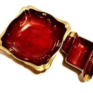 May include: A deep red, square-shaped bowl with a scalloped gold rim, paired with a smaller, rectangular red and gold tray featuring two integrated side rests. Both pieces have a glossy, smooth finish and a distinct, ornate metallic border.