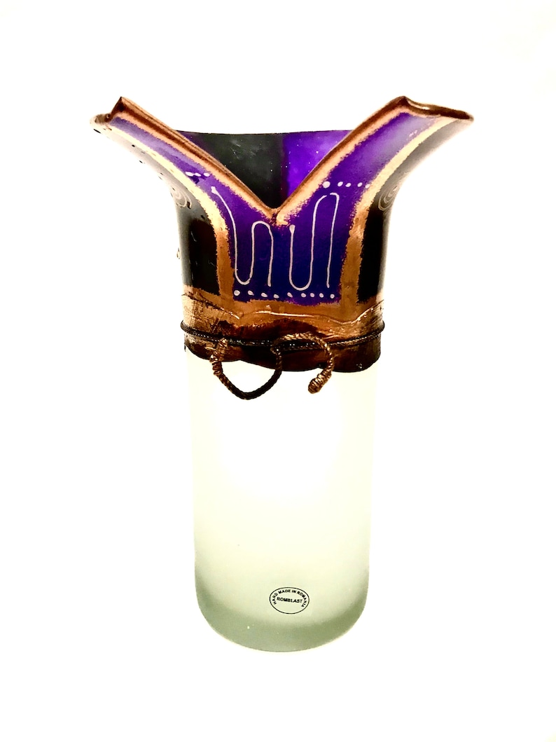 May include: A frosted glass vase with a flared, decorative top. The top features a purple and gold design with white accents. The vase has a cylindrical shape and a decorative wire detail around the middle.