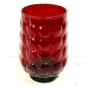 May include: A ruby red glass tumbler with a textured, bubble-like pattern. The glass has a dark base and a wide opening. This vintage-style drinking glass is suitable for water, juice, or cocktails.