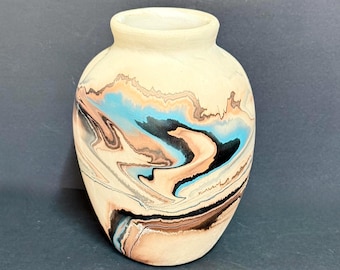 May include: A ceramic vase with a rounded body and a narrow neck, featuring a marbled surface pattern in shades of cream, light brown, black, and bright blue. The finish appears matte, and the swirling colors create a fluid, organic design.