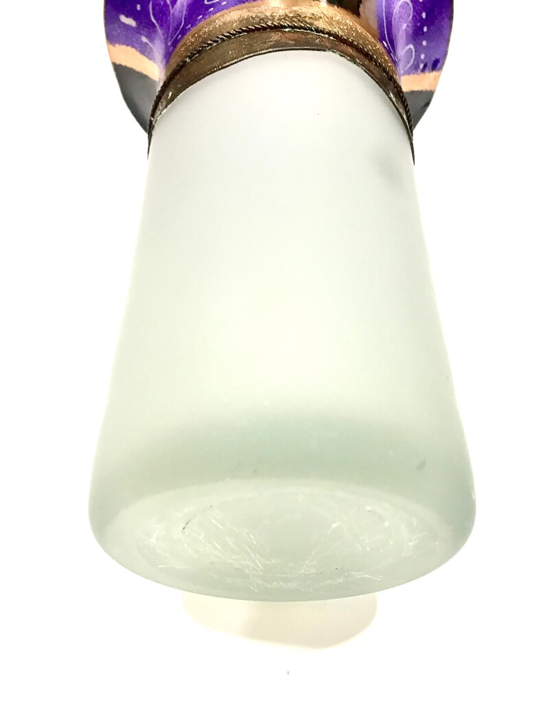 May include: A frosted glass lampshade with a decorative purple and gold top. The lampshade has a conical shape and a textured surface. The top features a decorative design with purple and gold accents.