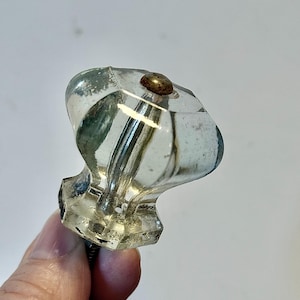 May include: Clear glass cabinet knob with a faceted design and a brass-colored screw head. The knob has a vintage aesthetic and is held by a hand against a white background. The knob is approximately 2 inches long.