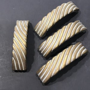 May include: Four antique brass drawer pulls with a twisted rope design. The pulls are rectangular with a series of diagonal grooves, creating a textured surface. One pull is positioned vertically, while the others are horizontal.