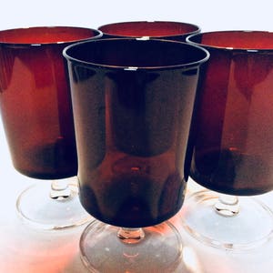 May include: Four dark red wine glasses with clear stems and bases. The glasses are arranged in a square formation.