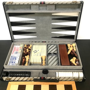 May include: A multi-game set featuring a backgammon board, chess board, playing cards, dominoes, and chess pieces. The backgammon board is open, revealing black and white triangles. The set includes a wooden chess board with a light and dark checkerboard pattern.