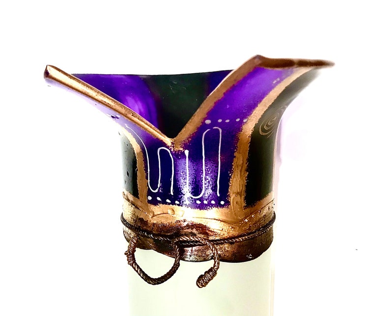 May include: A decorative, hand-painted vase with a flared top. The vase features a deep purple interior, outlined with gold and black accents. White, stylized patterns adorn the exterior, and a rope-like detail encircles the base.