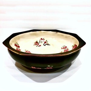 May include: A dark green ceramic bowl with a cream-colored interior. The bowl features a gold rim and is decorated with red floral patterns. The bowl has an octagonal shape and is likely used for decorative purposes.