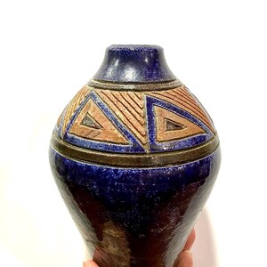 May include: A ceramic vase with a glossy deep blue glaze and a wide, rounded body. The upper section features a band of incised geometric triangle patterns in a matte terracotta brown finish, separated by dark brown horizontal ridges.