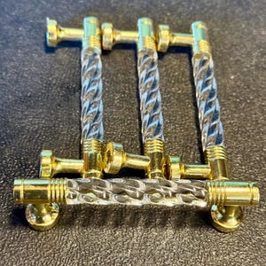 May include: A set of four cabinet pulls. Each pull features a clear, twisted acrylic center with gold-toned metal accents. The pulls are arranged in a row, showcasing their decorative design and hardware.