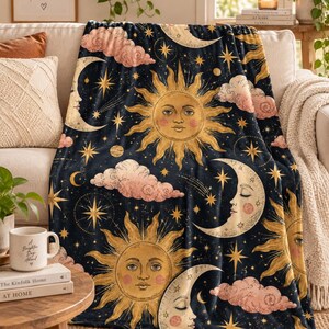 May include: A plush throw blanket featuring a dark navy blue background with a repeating celestial pattern of golden suns with human faces, cream-colored crescent moons with closed eyes, scattered yellow stars, and soft pink fluffy clouds.