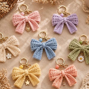 May include: Seven crochet bow keychains in various colours including pink, lavender, cream, blue, sage green, yellow, and peach. Each keychain features a gold-tone metal ring, a small coloured bead, and a unique charm like a heart, flower, or star.