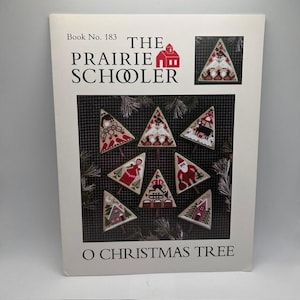 May include: A cross-stitch pattern booklet titled The Prairie Schooler Book No. 183 O Christmas Tree. The cover features a grid background with seven triangular ornaments displaying various holiday motifs in red, white, and black thread.