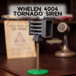 May include: A gray model of a Whelen 4004 Tornado Siren featuring a rectangular speaker housing with four horizontal horn projections. The model is mounted on a thin brown pole attached to a circular green base. The text Whelen 4004 Tornado Siren is visible.