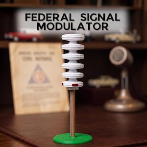 Peut inclure: Un modèle de Federal Signal Modulator blanc composé d'une pile verticale de six disques circulaires étagés, monté sur un poteau en bois avec une base circulaire verte. Le disque inférieur présente de petits accents rectangulaires rouges.