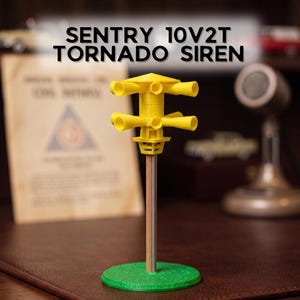 May include: A yellow SENTRY 10V2T TORNADO SIREN model featuring two tiers of horns mounted on a central pole with a green circular base. The siren has a pointed top cap and a detailed housing structure, standing upright as a scale replica display piece.