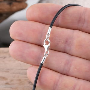 Sterling silver clasp on black leather necklace held in hand.