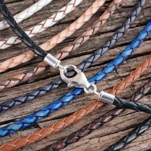 Braided leather necklaces in various colors with metal clasps are displayed on a wooden surface.