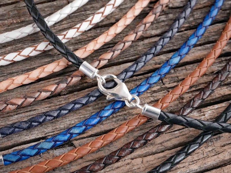 Braided leather necklaces in various colors with metal clasps are displayed on a wooden surface.