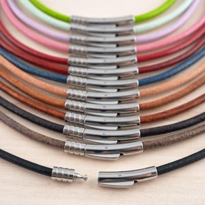 May include: A close-up of a variety of leather cord necklaces with silver clasps. The cords are arranged in a semi-circle, with the clasps facing the viewer. The cords are in various colors, including black, brown, tan, and green.