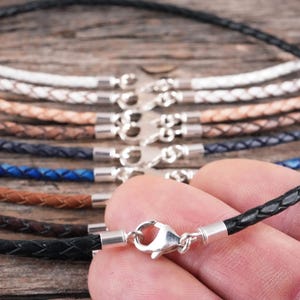 A braided black leather necklace being held in hand to show scale.