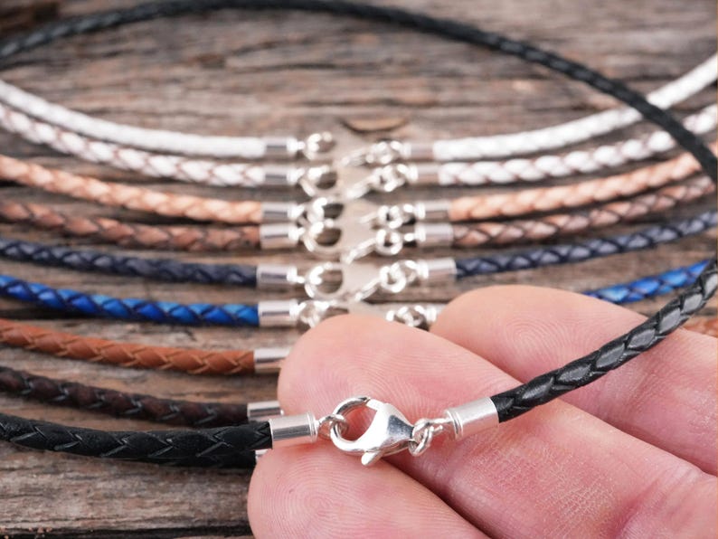 A braided black leather necklace being held in hand to show scale.