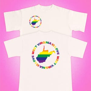 以下が含まれることがあります： オフホワイトの半袖Tシャツ。ウエストバージニア州の虹色の地図が円形のテキストデザインの中に配置されており、WEST VIRGINIA IS LOVEと書かれています。このデザインは胸元に小さく、背面に大きくプリントされています。