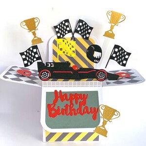 May include: A pop-up card featuring a black racing car, chequered flags and gold trophies. The card reads "Happy Birthday" in red lettering.