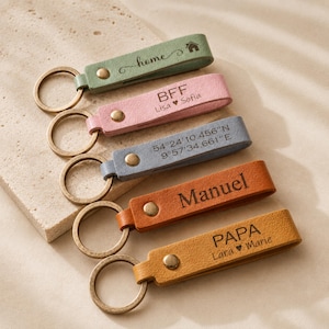 May include: Five leather keychains in sage green, light pink, slate blue, tan, and mustard yellow. Each features a metal ring, a gold-tone rivet, and custom laser-engraved text including home, BFF Lisa and Sofia, coordinates, Manuel, and PAPA Lara and Marie.