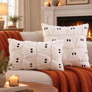 May include: Two white scatter cushions featuring a repeating tufted ghost pattern with black embroidered eyes. One cushion is square and the other is rectangular. Both cushions have a textured, plush surface design against a solid white fabric base.