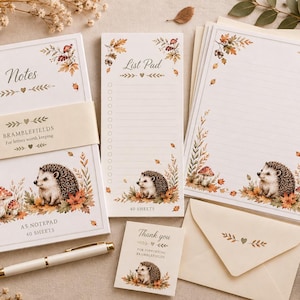 May include: A stationery set featuring a hedgehog and autumn leaf illustration. Includes an A5 notepad with 40 sheets, a list pad with 40 sheets, lined writing paper, a cream envelope, and a small thank you card, all accompanied by a white pen.