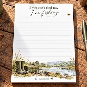 May include: A white lined notepad featuring the text If you can't find me, I'm fishing at the top. The bottom displays a colorful illustration of a river landscape with fishing boots, a tackle box, a mug, and a fishing rod.
