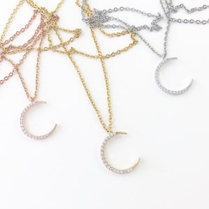 May include: Three delicate necklaces with crescent moon pendants adorned with sparkling cubic zirconia stones. The necklaces are available in gold, rose gold, and silver.
