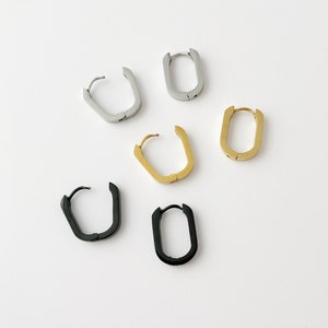 May include: Five pairs of hoop earrings in different colours. The earrings are made of metal and have a rectangular shape. The colours are silver, gold, and black.