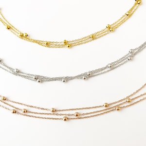 May include: Three layered necklaces with small beads. The necklaces are gold, silver, and rose gold.