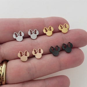 May include: Six pairs of small, silver, gold, rose gold, and black stud earrings featuring a cutout design of a cartoon mouse head with a bow.